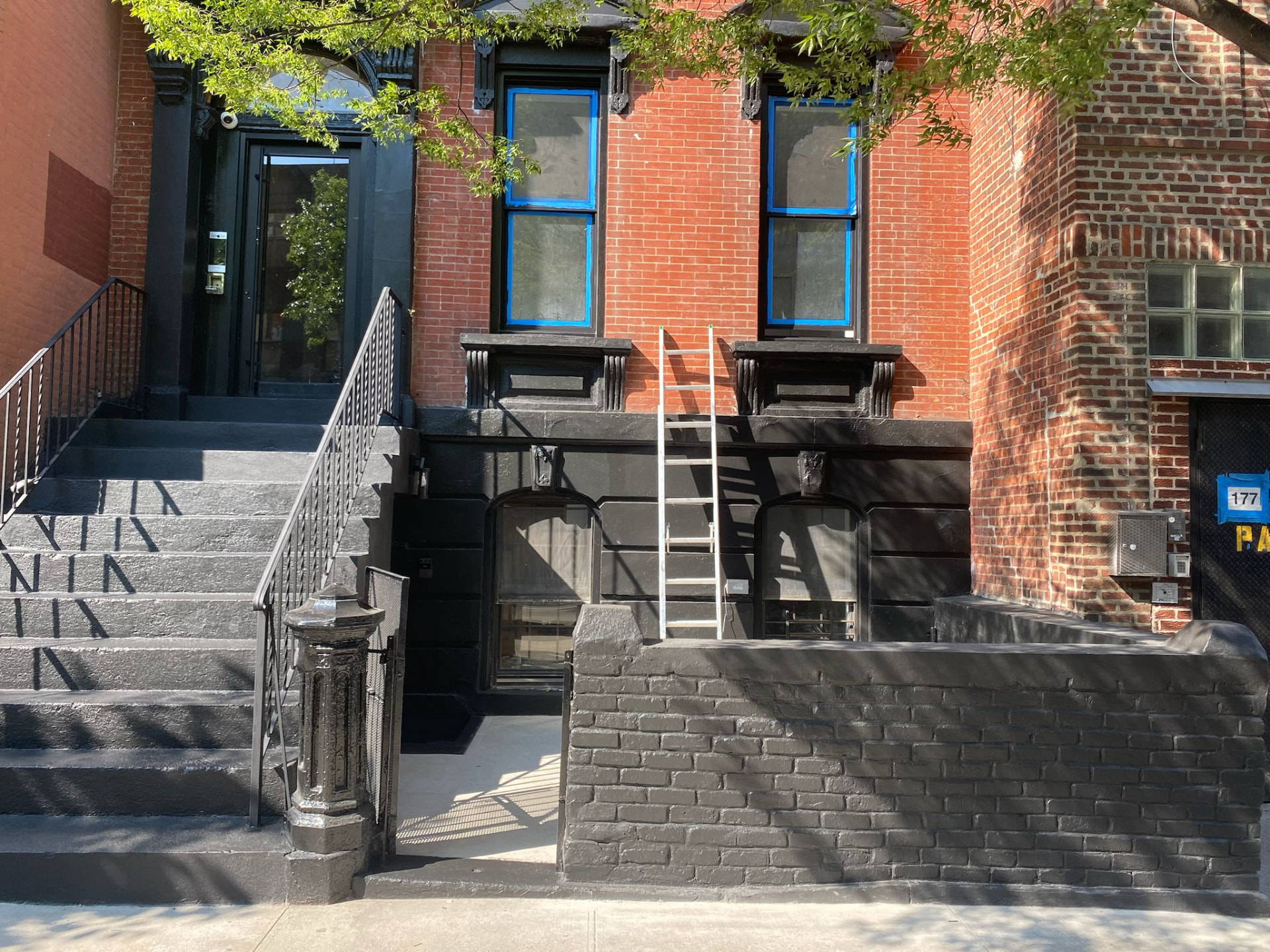 Brownstone facade restoration in progress with fresh black masonry finish and protected windows