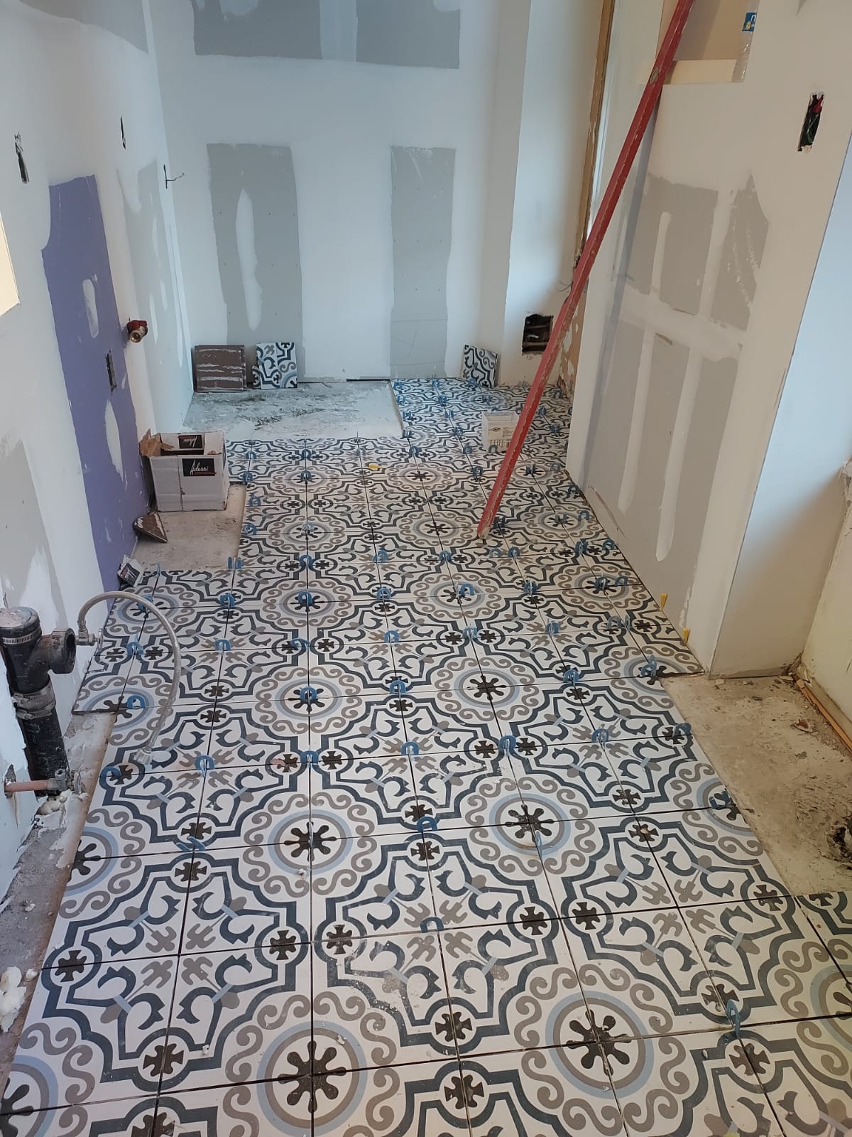 Patterned floor tile installation in progress with tile spacers and unfinished sheetrock walls