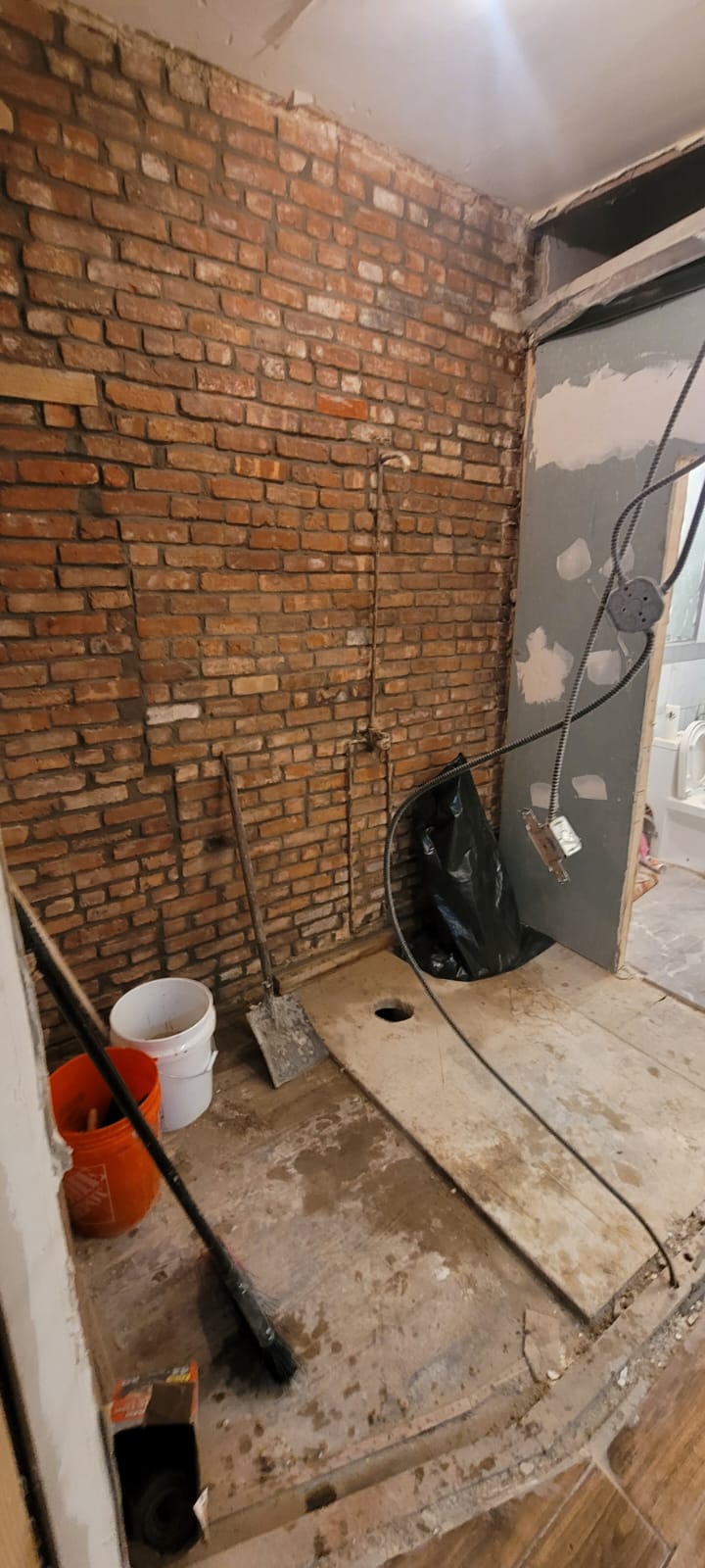 Interior renovation before finish work, with exposed brick, unfinished floor and open utility lines